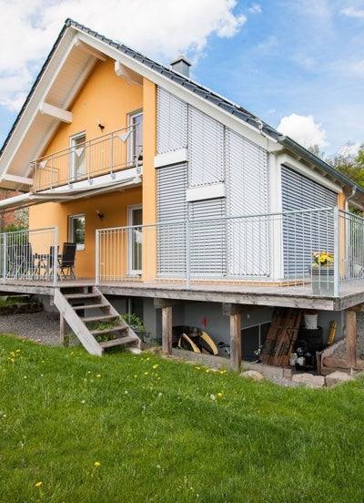 Geländer "Ancona" in feuerverzinkt um ein gelbes Haus auf einer Holzterrasse montiert